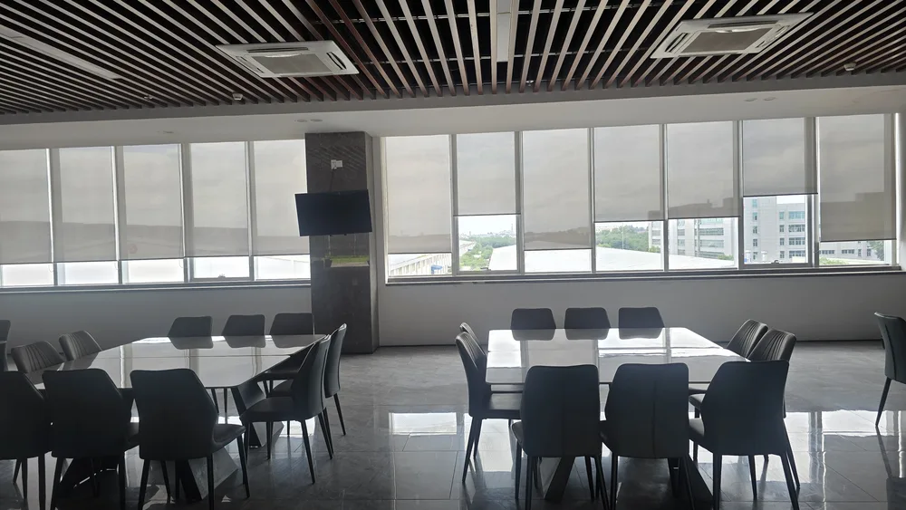 Sun-blocking roller blinds installed across the entire glass facade of an office building canteen